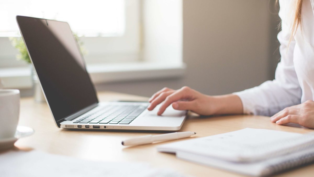 Close-up of a person's hands typing on a laptop at a desk with a notebook and pen, soft neutral tones, calm productive mood