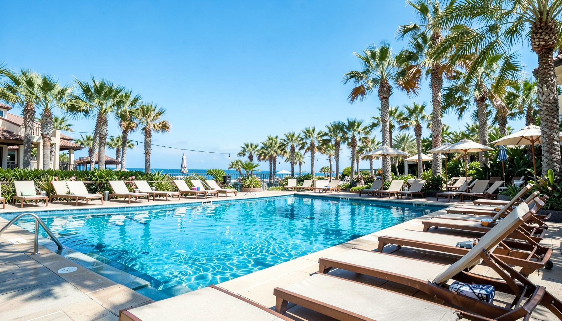 Resort poolside with lounge chairs and palm trees under a clear blue sky, relaxed vacation atmosphere